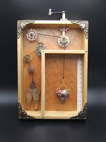 Mixed media wooden shadow box  Blown glass heart and metal wings attached together by metal gears and a string  Gear handle on top of the piece  Pieces are not movable  7.75" long x 5.5" wide x 1.5" high
