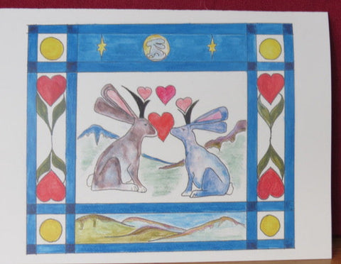 Two Jackalope with hearts between them and mountains in the background  Blue boarder with heats, greenery, along with moon, mountains, and stars  4" long x 5 1/2" high blank card with envelope  Great Valentine's Day card for the ones you love. Design is from an original drawing by the artist.