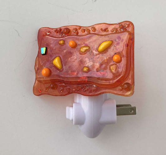 used Glass Nightlight  Orange glass fused to orange glass with orange and yellow glass plus a small gold colored embellishment  3" long x 2" high x 1/4" wide fused glass  Total height of glass and nightlight is 3"  2 prong plug 